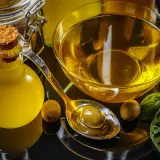 Botella de aceite de oliva, cuenco con aceite, cuchara con aceituna y hojas de albahaca. El precio del aceite de oliva va a subir.
