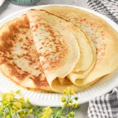 Deliciosos crepes sin gluten apilados en un plato blanco, con un toque de flores amarillas y una servilleta a cuadros.