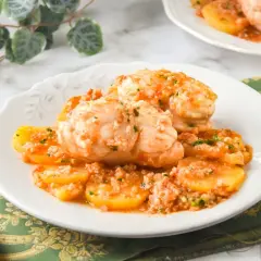 Rape con patatas en salsa de tomate, servido en plato blanco con tenedor y pan.