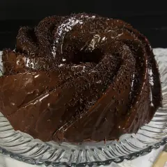 Bizcocho de chocolate glaseado y cubierto con chispas de chocolate, servido en un plato de cristal.