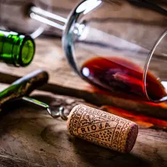 Tapón de corcho con la inscripción "Rioja" y "Calificación Añada", junto a una botella y copa de vino tinto sobre madera.