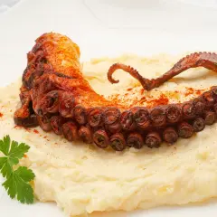 Delicioso pulpo a la plancha con puré cremoso, espolvoreado con pimentón y adornado con perejil fresco.