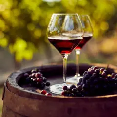 Dos copas de vino tinto y uvas moradas sobre un barril de madera, evocando las mejores añadas de vino.