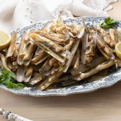 Deliciosas navajas a la plancha servidas en una fuente con limón y perejil.
