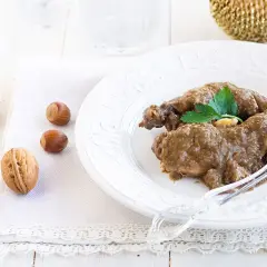 Delicioso conejo al ajillo servido en un plato blanco, acompañado de nueces y avellanas.