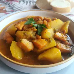 Un reconfortante plato de sepia con patatas, trozos de patata y zanahoria en una sabrosa salsa, adornado con perejil fresco.