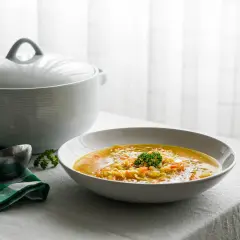 Un plato humeante de sopa juliana, con verduras cortadas finas y un toque de perejil, listo para servir desde una olla blanca.