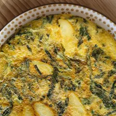 Tortilla de acelgas casera, dorada y jugosa, con trozos de patata y hojas verdes integradas en el huevo.