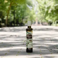 Aceite de oliva virgen extra de la almazara Pago de Valdecuevas, en botella oscura, sobre un camino de baldosas con árboles al fondo.