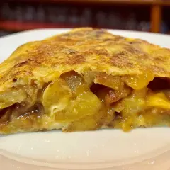 Rebanada de tortilla de patatas jugosa, con trozos dorados de patata y huevo.