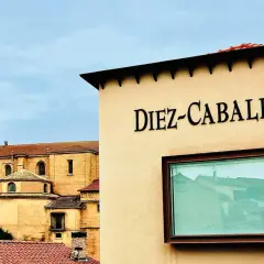 Edificio con el nombre "Diez-Caballero" en relieve, con una iglesia antigua al fondo.
