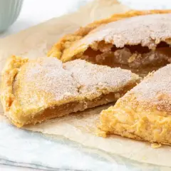 Un delicioso pastel cordobés, espolvoreado con azúcar, con una porción cortada mostrando su relleno dorado.