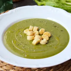 Crema de acelgas verde vibrante, servida en plato blanco con picatostes dorados y un chorrito de aceite de oliva.