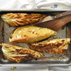 Cuatro gajos de col asada en una bandeja metálica, con hierbas y bordes dorados. Perfectas para tus recetas con col.