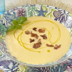 Deliciosa crema de espárragos, coronada con crujientes trocitos de jamón y un hilo de aceite de oliva. Servida en un plato con motivos marinos.