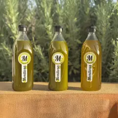 Tres botellas de aceite de oliva virgen extra Monttosa, con etiquetas amarillas y verdes, reposan sobre una superficie de piedra ante un fondo de vegetación.