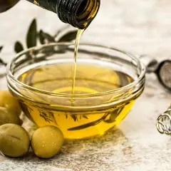 Aceite de oliva virgen extra vertiéndose en un cuenco, rodeado de aceitunas y hierbas. Un tesoro de vitaminas del aceite de oliva.