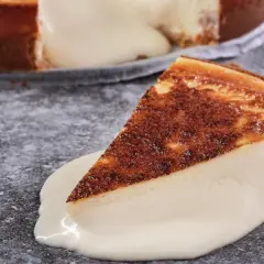Una porción de tarta de queso cremosa, con la base dorada y el relleno blanco, se desliza sobre una salsa de queso.