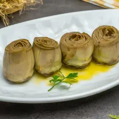 Cuatro alcachofas confitadas en aceite de oliva, servidas en plato blanco con perejil.