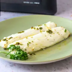 Dos filetes de merluza jugosa, recién hechos en airfryer, con hierbas frescas y aceite de oliva.