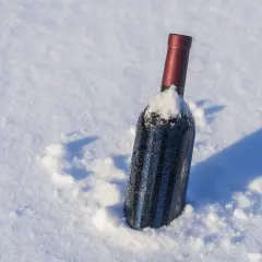Botella de vino tinto cubierta de nieve, parece que el vino se congela en la nieve.