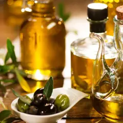Aceite de oliva dorado en botellas y jarra, con aceitunas frescas y ramas de olivo. Descubre las propiedades del aceite de oliva.