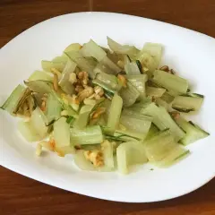 Pencas de acelgas salteadas con nueces, servidas en un plato blanco sobre una mesa de madera.