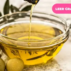 Aceite de oliva vertiéndose en un cuenco, rodeado de aceitunas y hojas de olivo. Descubre los múltiples usos del olivo.