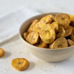 Un tazón de crujientes rodajas de plátano frito, espolvoreadas con sal, listas para disfrutar.