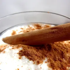 Vaso de leche merengada con canela en polvo y una rama de canela.