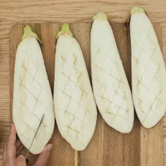 Berenjenas cortadas a la mitad, listas para ser rellenas. A su lado, ajos, albahaca, sal y pimienta.