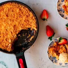 Crumble de manzana recién horneado en sartén, servido en platos con fresas y helado. ¡Un postre casero irresistible!