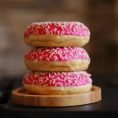 Tres deliciosos donuts caseros apilados, cubiertos con glaseado rosa brillante y chispas blancas.