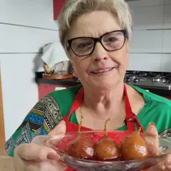 Mujer sonriente muestra un plato con peras al vino, un postre casero listo para disfrutar.