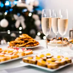 Copas de vino frizzante listas para brindar junto a aperitivos festivos, con un árbol de Navidad decorado al fondo.