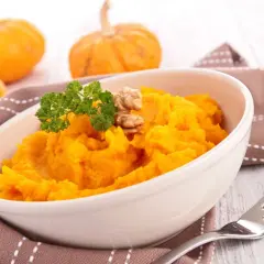 Un tazón de cremoso puré de calabaza, decorado con perejil y nueces, junto a calabazas pequeñas.