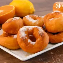 Rosquillas de naranja recién hechas, espolvoreadas con azúcar, junto a naranjas y un limón.
