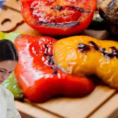 Chef preparando pimientos asados, tomates y champiñones a la parrilla en una tabla de madera.