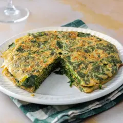 Tortilla de espinacas, jugosa y dorada, servida en plato blanco con servilleta a cuadros.