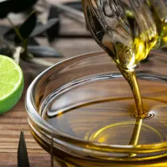 Aceite y limón en ayunas: conoce las contraindicaciones. Se ve aceite vertiéndose en un cuenco, junto a limones frescos.