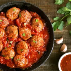 Sabrosas albóndigas en salsa roja, servidas en una sartén de hierro fundido, con perejil fresco y especias al lado.