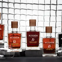 Cinco botellas de brandy de Jerez de la colección Altanza, incluyendo un amontillado, dispuestas sobre una superficie oscura con copas de vino vacías.