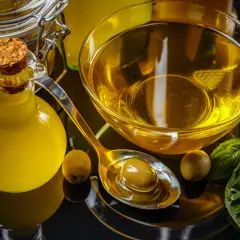 Botella de aceite de oliva, cuenco con aceite, cuchara con aceituna y hojas de albahaca. El precio del aceite de oliva va a subir.