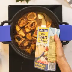Se añade caldo de pescado a una cazuela con calamares y patatas, ingredientes para una deliciosa caldereta.