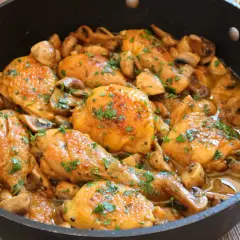Pollo a la cerveza jugoso y dorado, con champiñones y perejil picado, servido en una sartén.