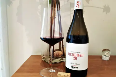 Una copa de vino tinto junto a una botella de vino del Bierzo. El corcho yace cerca, listo para otra degustación.