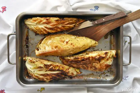 Cuatro gajos de col asada en una bandeja metálica, con hierbas y bordes dorados. Perfectas para tus recetas con col.