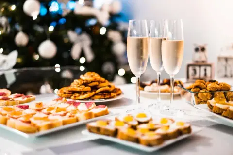 Copas de vino frizzante listas para brindar junto a aperitivos festivos, con un árbol de Navidad decorado al fondo.