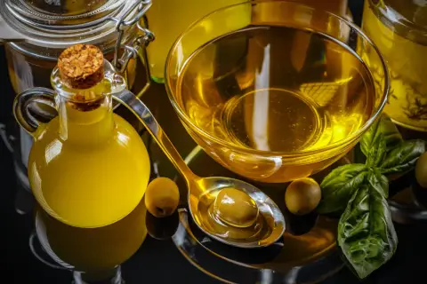 Botella de aceite de oliva, cuenco con aceite, cuchara con aceituna y hojas de albahaca. El precio del aceite de oliva va a subir.