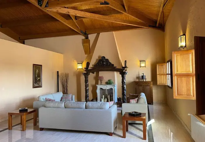 Salón acogedor en finca Los Aljibes, con chimenea rústica, sofás cómodos y vigas de madera en el techo.